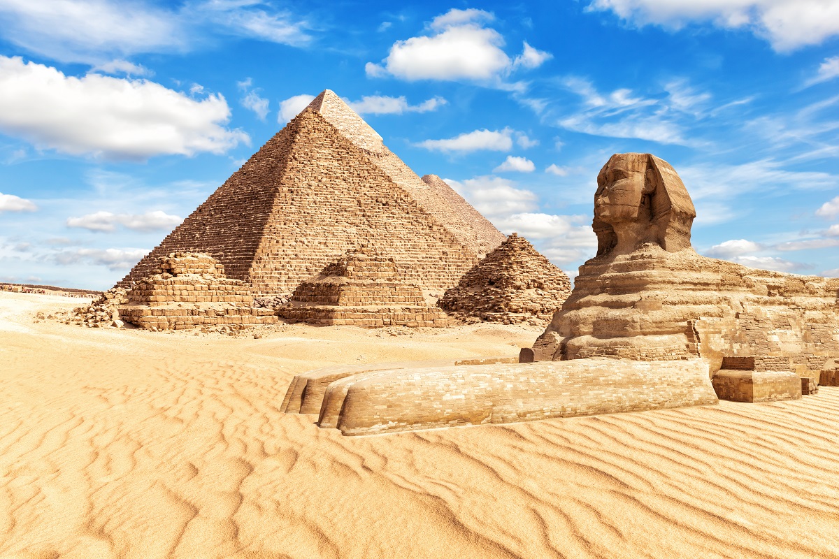 Piramidele din Giza și celebrul Sfinx, construite în deșert, cu cerul albastru pe fundal