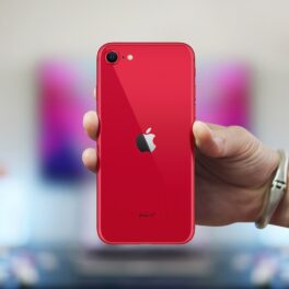 Smartphone Apple iPhone SE 2020, unul dintre cele mai bune smartphone-uri cu prețuri accesibile, cu o carcasă roție, ținut în mână