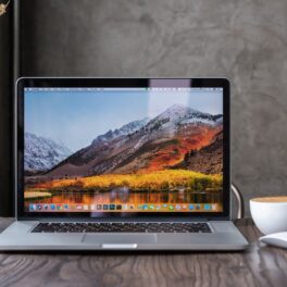 Calculator Macbook pro, pe un birou din lemn închis la culoare, deschis, cu un mouse alb lângă. Apple ar putea lansa 5 calculatoare Mac în 2022