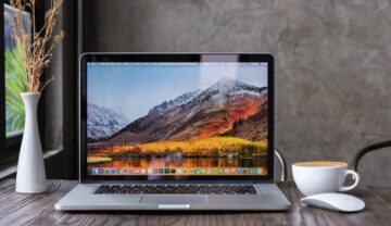 Calculator Macbook pro, pe un birou din lemn închis la culoare, deschis, cu un mouse alb lângă. Apple ar putea lansa 5 calculatoare Mac în 2022