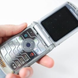 Telefon Motorola RAZR argintiu ținut în mână de un utilizator, pe fundal alb. Butonul Motorola RAZR pentru Internet se afla deasupra butonului de răspuns apel