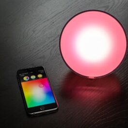 Philips Hue Lights, lângă un telefon mobil, pe un fundal negru, cu o lumină roz. Philips Hue Lights se numără printre cele mai bune dispozitive din 2021