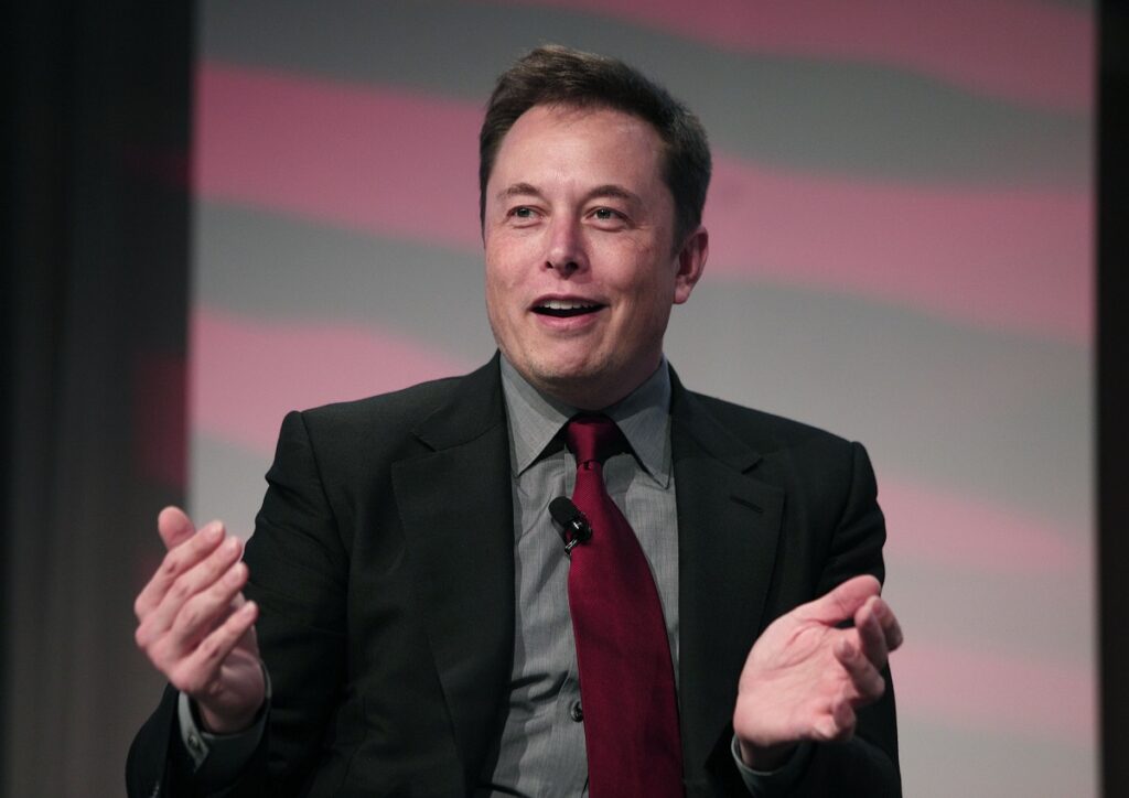 Elon Musk, la evenimentul Automotive News World Congress, ianuarie 2015. Vorbește, e îmbrăcat într-un costum negru, cu o cămașă gri și o cravată roșie. Descoperirea din curtea fabricii lui Elon Musk a atras atenția fanilor