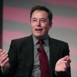 Elon Musk, la evenimentul Automotive News World Congress, ianuarie 2015. Vorbește, e îmbrăcat într-un costum negru, cu o cămașă gri și o cravată roșie. Descoperirea din curtea fabricii lui Elon Musk a atras atenția fanilor