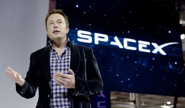 Elon Musk, pe scenă, la un eveniment SpaceX, când a dezvăluit nava The Dragon V2, în 2014. Logo-ul SpaceX se află în spatele lui, el e îmbrăcat în costum negru. Elon Musk a fost criticat de cetățenii chinezi din cauza proiectului Starlink