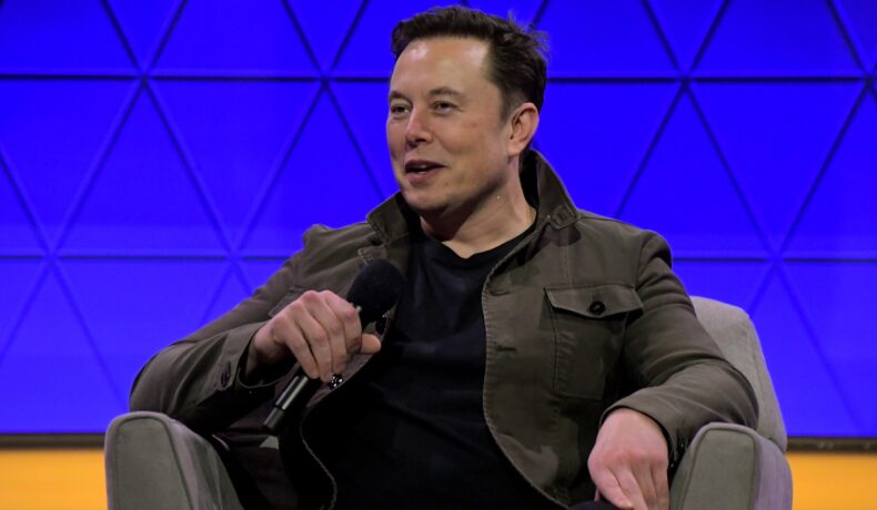 Elon Musk, pe scena E3 2019. Stă ântr-un fotoliu gri, are o bluză neagră și un fundal albastru. Elon Musk vrea să creeze combustibil din dioxid de carbon