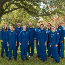 Noua clasă de astronauți NASA, poză oficială, din 6 decembrie 2021. 10 oameni, care poartă costume albastre, pe un fundal cu verdeață