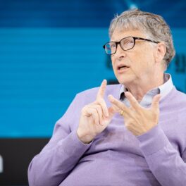 Bill Gates, anul 2019, pe scenă la evenimentul New York Times Dealbook, din New York. Îmbrăcat într-o bluză mov deschis, cu fundal albastru în spate. Bill Gates a vorbit despre planurile lui pentru 2022