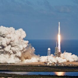 Lansare de rachetă, creată din elemente oferite de NASA, cu o rachetă albă, care lasă în urmă un nnor de fum, pe fundal se văd marea și cerul, albastre. SpaceX a doborât un record cu 2 misiuni