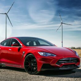 Mașina roșie Tesla Model S, în fața unor turbine de vânt, cu cer albastru pe fundal. Tesla recheamă în service aproape 500.000 de mașini