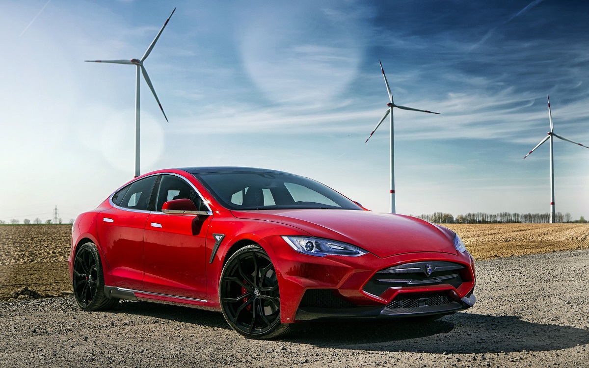 Mașina roșie Tesla Model S, în fața unor turbine de vânt, cu cer albastru pe fundal. Tesla recheamă în service aproape 500.000 de mașini