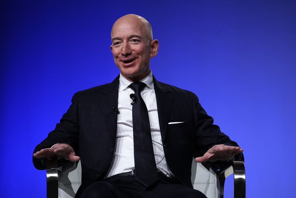 Jeff Bezos, fondatorul Amazon, pe scena conferinței Air Force Association, din 2018. Poartă un costum negru și o cămașă albă, pe un fundal albastru. Trucul lui Jeff Bezos crește productivitatea