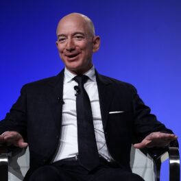 Jeff Bezos, fondatorul Amazon, pe scena conferinței Air Force Association, din 2018. Poartă un costum negru și o cămașă albă, pe un fundal albastru. Trucul lui Jeff Bezos crește productivitatea