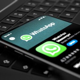 Telefon care are aplicația WhatsApp pe ecran, carcasă neagră. Telefonul e pe o tastatură Windows. WhatsApp va fi lansată pe Windows 11 și 10
