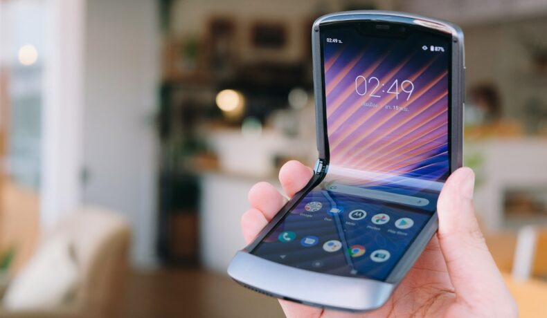 Telefonul Motorola RAZR 5G, lansat în anul 2020, ținut în mână de un utilizator, cu fundal de cameră. Varianta Motorola RAZR 5G nu mai are butonul de Internet