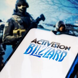 Logo-ul Activision Blizzard pe ecranul unui telefon, cu un joc video pe fundal, cu arme