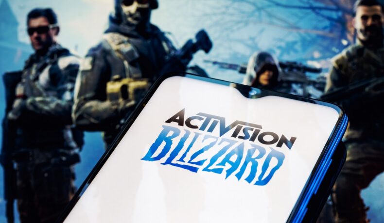 Logo-ul Activision Blizzard pe ecranul unui telefon, cu un joc video pe fundal, cu arme