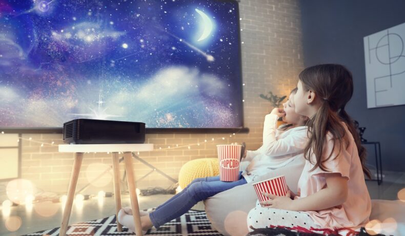 Videoproiector negru, care arată o imagine pe perete, în camera unor copii. Doi copii se uită la un ecran înstelat. Videoproiectorul Samsung a atras atenția la CES 2022