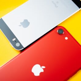 Telefon iPhone SE alături de un iPhone 8, unul roșu, altul alb, pe un fundal galben. iPhone SE a fost anunțat în 2020