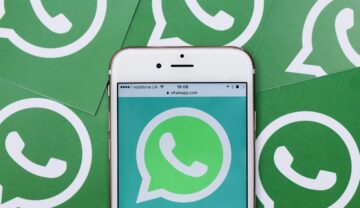 Logo WhatsApp pe un telefon alb, cu multe logo-uri ale aplicației pe fundal. Există trucuri prin care îți poți proteja contul WhatsApp