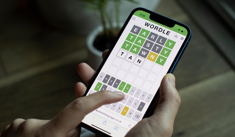 Utilizator care are un telefon cu jocul Wordle pe ecran. Poți juca Wordle de mai multe ori dacă accesezi arhiva