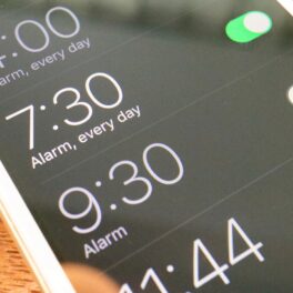 Ecran iPhone, cu meniul de alarme, pe o masă din lemn. Telefoanele iPhone au durata de snooze de 9 minute