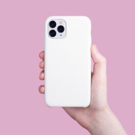 iPhone 11 Pro cu o husă albă, ținut în mână, pe un fundal roz. Unii experți recomandă să nu folosești telefonul fără husă
