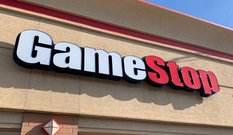 Semn al unui magazin GameStop, cu roșu și alb, pe un fundal bej. GameStop ar putea fi afectat de anunțul Microsoft-Activision Blizzard