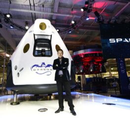 Elon Musk alături de cabina de navă The Dragon V2, SpaceX, în 2014, California. El poartă un costum negru, naveta e albă. Recent, Kyle Hippchen a câștigat o șansă să se afle într-una din aceste nave