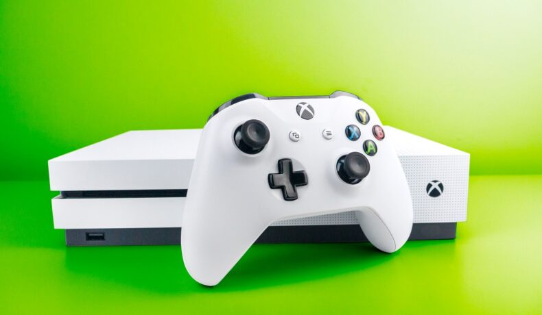 Consola Xbox One, pe alb, pe un fundal verde deschis. Microsoft a oprit recent producția pentru această consolă