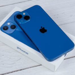 Telefon iPhone 13, pe albastru, pus pe cutia albă Apple, pe un fundal de lemn gri deschis. Designul iPhone 14 Pro ar putea fi foarte diferit