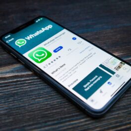 Telefon cu WhatsApp pe ecran, care se află pe o masă din lemn închis. Opțiunile WhasApp pe care utilizatorii trebuie să le schimbe în 2022 pot proteja datele