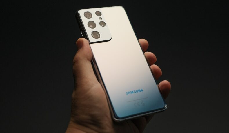 Samsung Galaxy S21 Ultra, pe argintiu, ținut în mână de un utilizator, pe un fundal negru. Primul teaser cu Samsung Galaxy S22 a fost lansat recent