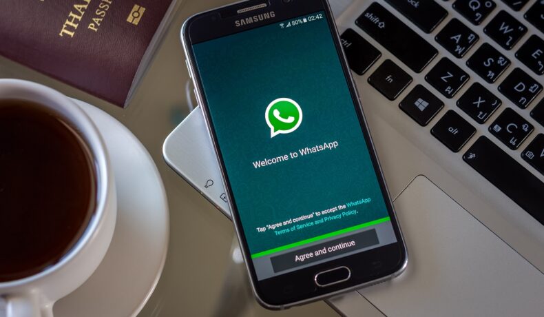Telefon care are WhatsApp pe ecran, care stă pe un laptop, lângă o ceașcă de cafea