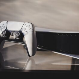 Consolă PlayStation 5, pe alb, pe un fundal gri cu negru. Consola e produsă de compania Sony, ce va produce mai multe console PS4 în 2022