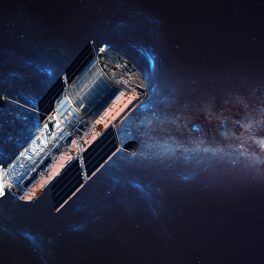 Telescopul Hubble, în spațiu, cu galaxii în spatele lui, pe fundal negru