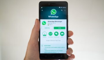 Telefon ținut în mână de un utilizator, pe fundal alb, cu aplicația WhatsApp pe ecran, ce ar putea permite mutarea conversațiilor în curând