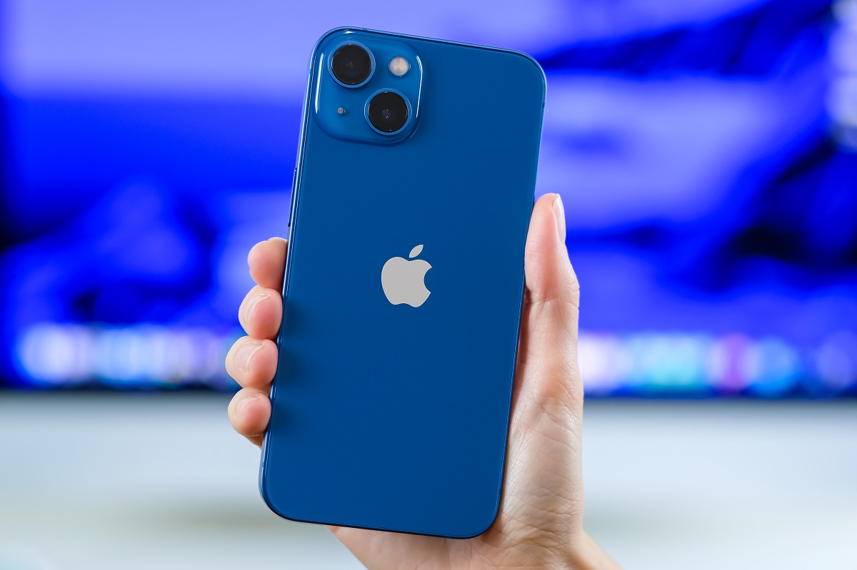 iPhone 13, pe albastru, ținut în mână de un utilizator, cu fundal albastru și alb