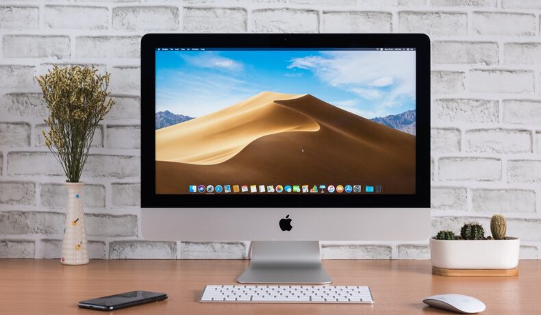 Minitor iMac, pe un birou, cu un perete alb în spate, și tastatură lângă el. Apple ar putea lansa un nou cip M2 în 2022