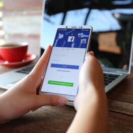 Utilizator care are Facebook deschis pe ecranul telefonului mobil, cu un laptop în spate. Capitalizarea de piață Facebook a scăzut sub 600 de miliarde