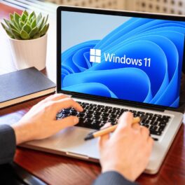 Utilizator care stă la birou, cu mâinile pe un laptop cu simbolul windows 11 pe ecran. Mulți utilizatori se întreabă cum activezi Modul Dumnezeu în Windows