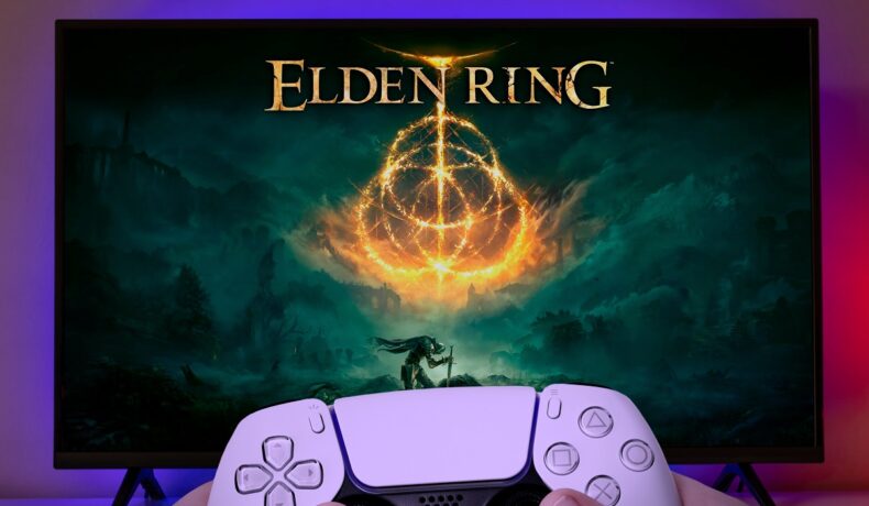 Monitor care are jocul Elden Ring pe ecran, cu un utilizator care ține un controller în mână în fața lui. Elden Ring a primit unele dintre cele mai bune recenzii din istorie