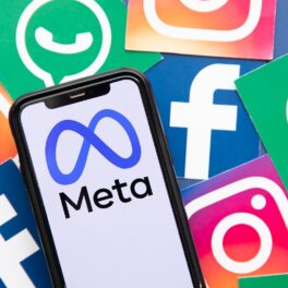 Telefon pe ecranul căruia apare logo-ul Meta, cu simbolurile Facebook, WhatsApp și Instagram pe fundal. Recent, Facebook a pierdut 500 de miliarde de dolari