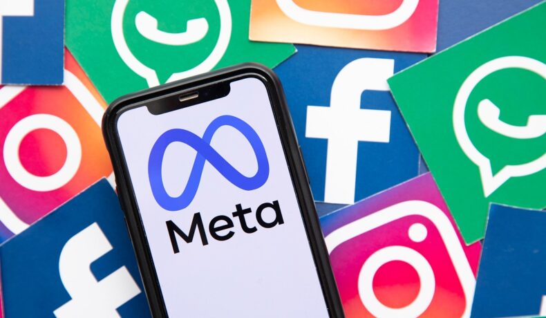 Telefon pe ecranul căruia apare logo-ul Meta, cu simbolurile Facebook, WhatsApp și Instagram pe fundal. Recent, Facebook a pierdut 500 de miliarde de dolari