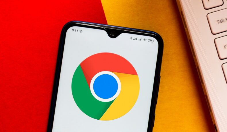 Logoul Google Chrome, înainte să fie schimbat, pe ecranul unui telefon mobil, lângă o tastatură