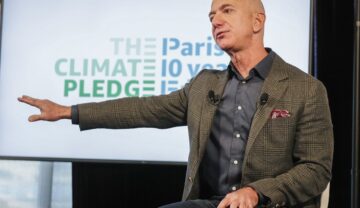 Jeff Bezos, pe scenă când a anunțat cofondarea The Climate Pledge, în 2019. Poartă o jachetă maro, cu o cămașă gri, pe fundal alb/ Iahtul lui Jeff Bezos costă 430 de milioane de euro