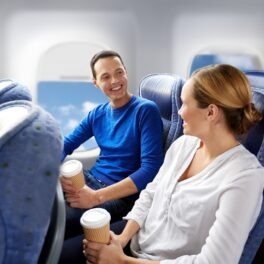 Doi pasageri de avion, care vorbesc unul cu altul și stau în scaun. El poartă o bluză albastră, ea o bluză albă. Atunci când vine vorba despre ce lucruri nu trebuie să le porți când călătorești cu avionul, există o listă