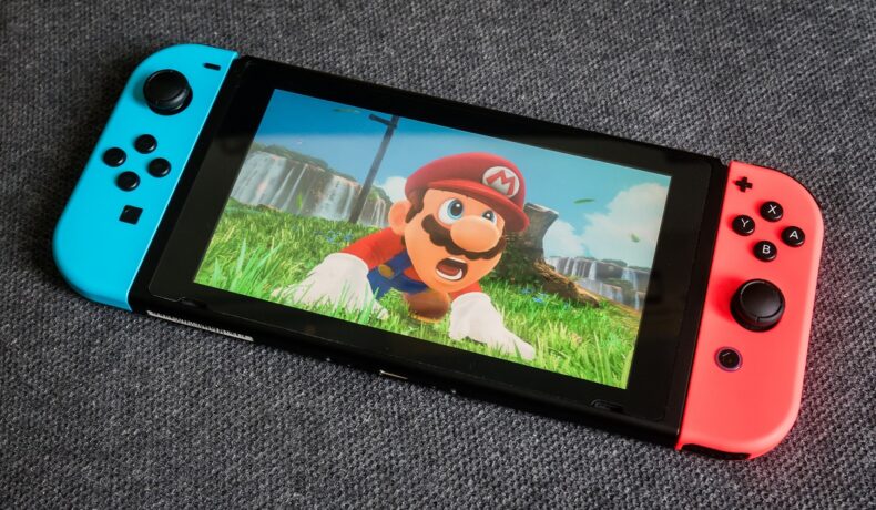 Consolă Nintendo Switch, cu o captură dintr-un joc Mario pe ecran, pe un fundal gri. Nintendo Direct din februarie 2022 a anunțat și o schimbare pentru Mario Kart
