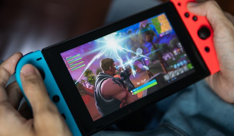 Dispozitiv Nintendo Switch, ce a vândut peste 100 de milioane de unități, în mâna unui utilizator, cu un joc pe ecran