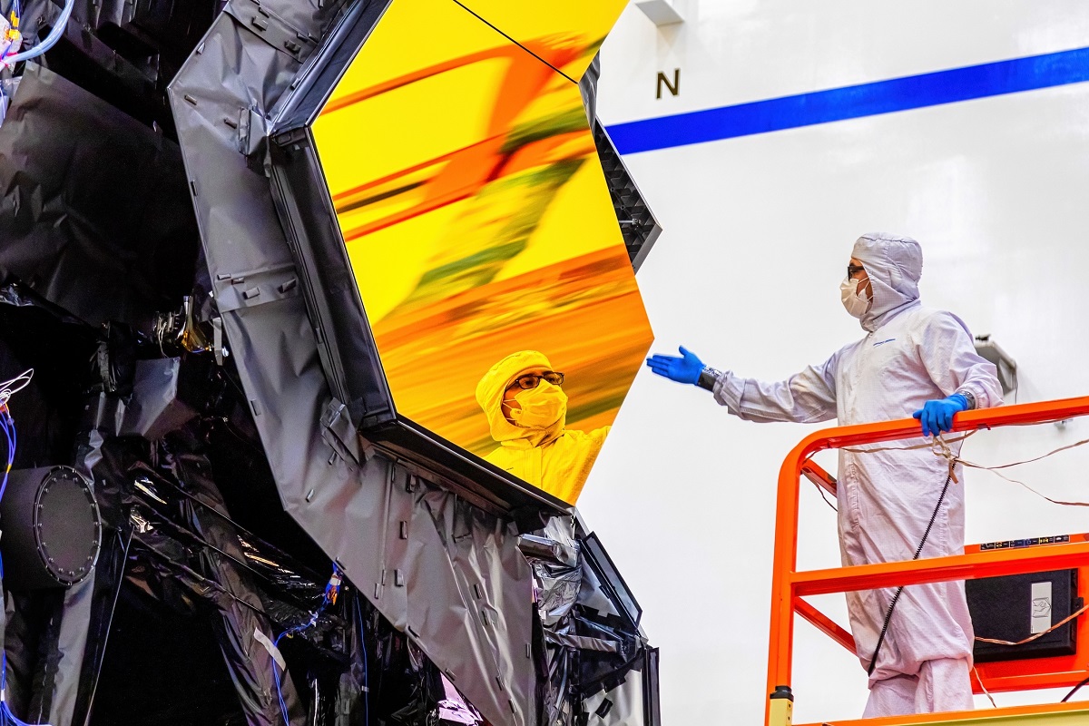 Un cercetător care se uită în oglinda galbenă a Telescopului James Webb, ce ar putea detecta viața extraterestră